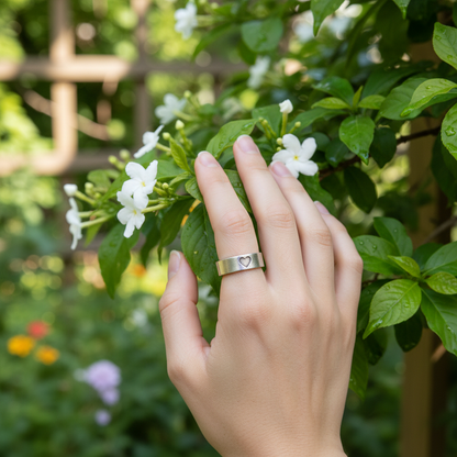 Hand wearing Hearts of Gold KIND heart ring touching flowers
