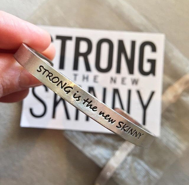 Person holding the Strong Is The New Skinny Quotable Cuff Bracelet