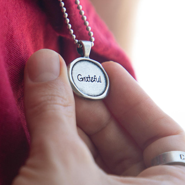 Person holding Grateful Wax Seal necklace