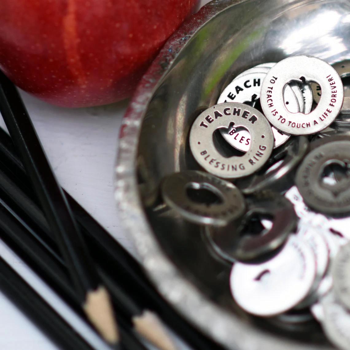 Teacher Blessing Rings in a bowl next to an apple and pencils